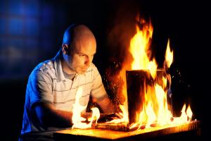 Image of a man using a laptop that is engulfed in flames